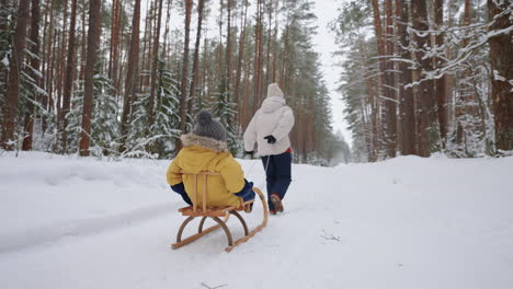 woman-is-running-in-winter-forest-and-pulling-sledge-with-her-little-son-happy-family-weekend